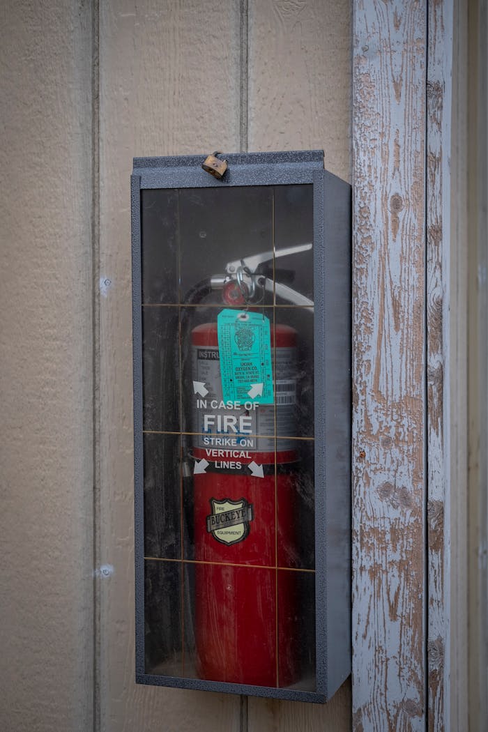 A red fire extinguisher enclosed in a glass case mounted on a wooden wall for safety.